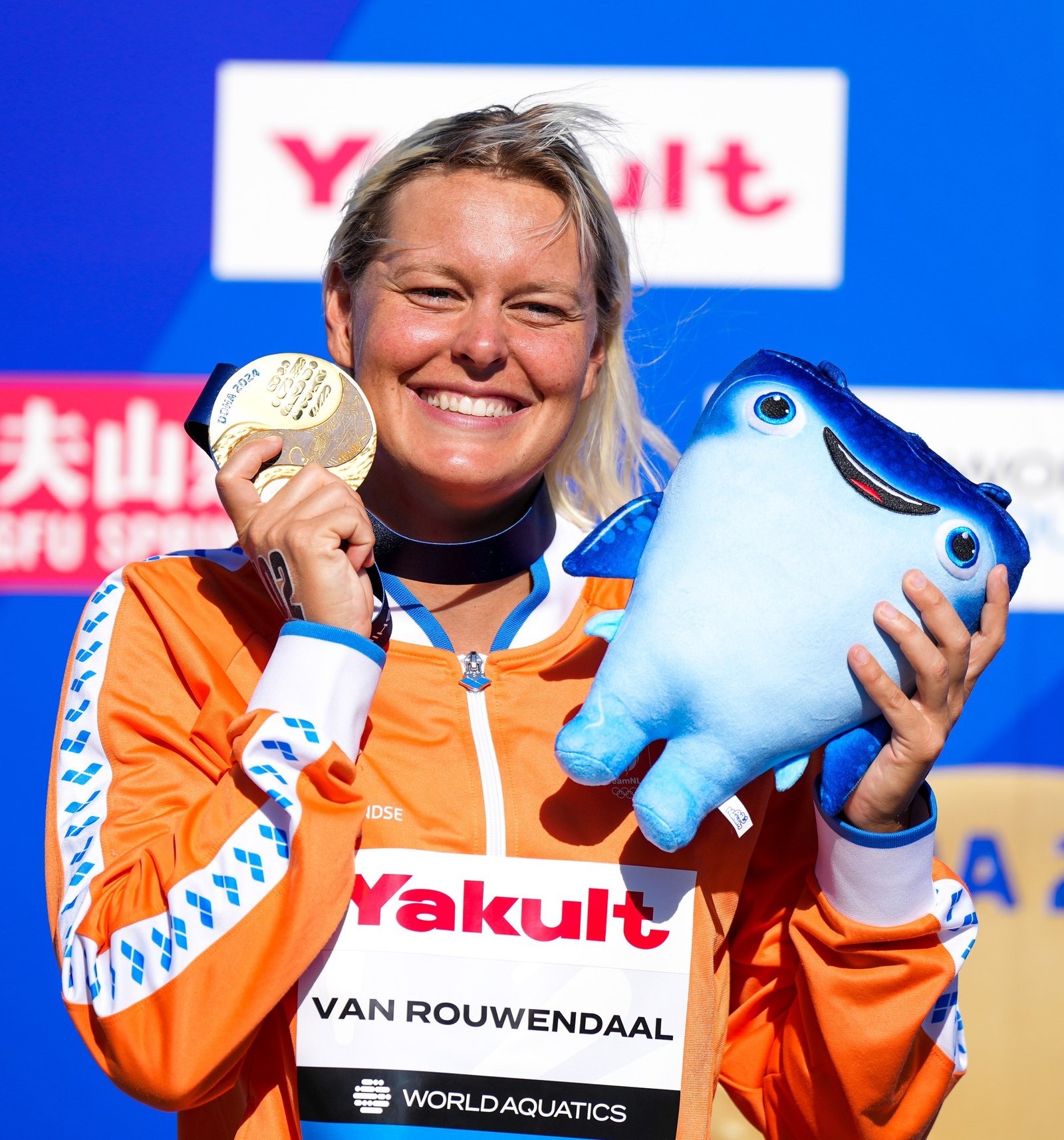 Sharon smiling with a gold medal and a blue mascot.